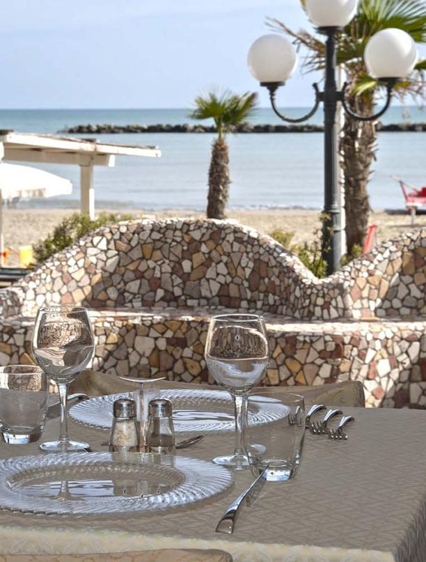 Tavolo apparecchiato con vista mare e bottiglie di vino.