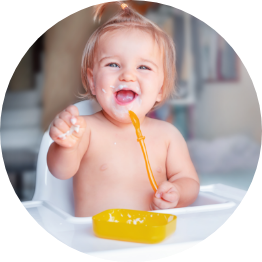 Happy baby eating with orange spoon.