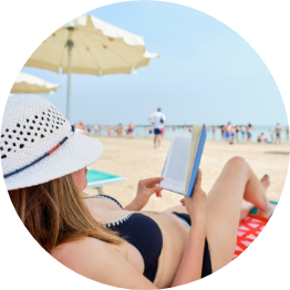 Woman reading on the beach under an umbrella.