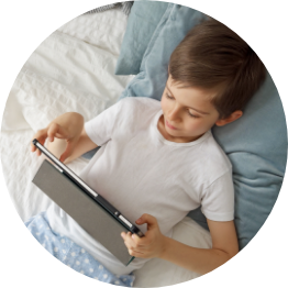 Child lying on bed using a tablet.